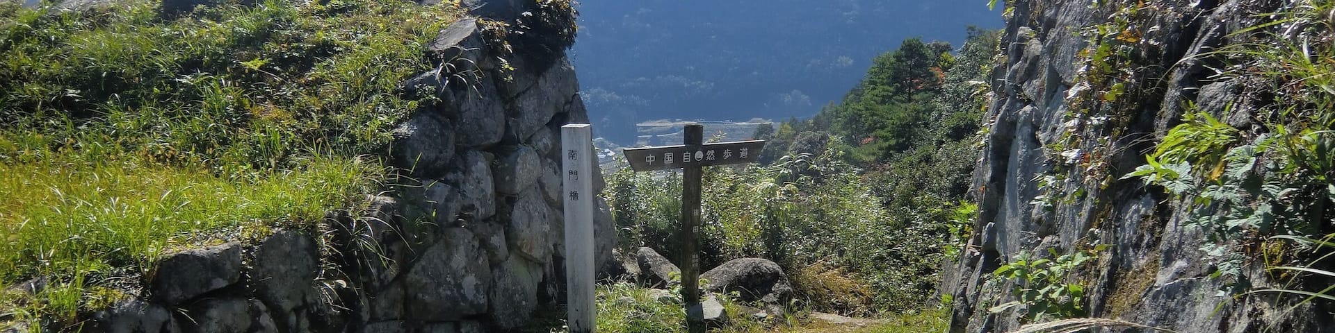 A stone pathway leading through a mountainous landscape with a signpost indicating directions.