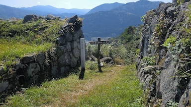 Un sendero de piedra serpentea por un paisaje montañoso con un indicador señalando las direcciones.