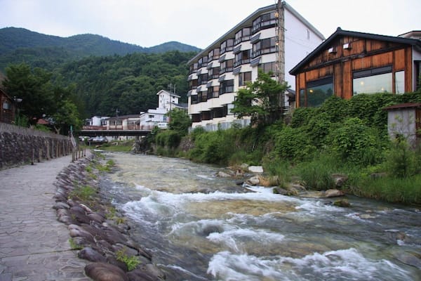 Ein Fluss fließt durch eine Stadt, gesäumt von Gebäuden, umgeben von grüner Natur und Bergen.