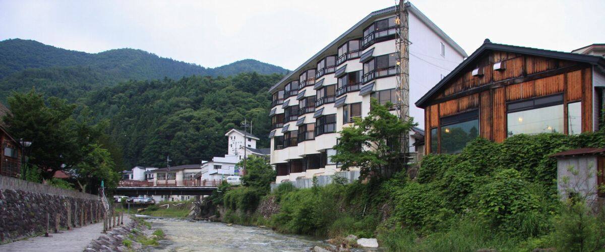 A river flowing through a town with buildings on both sides, surrounded by greenery and mountains.