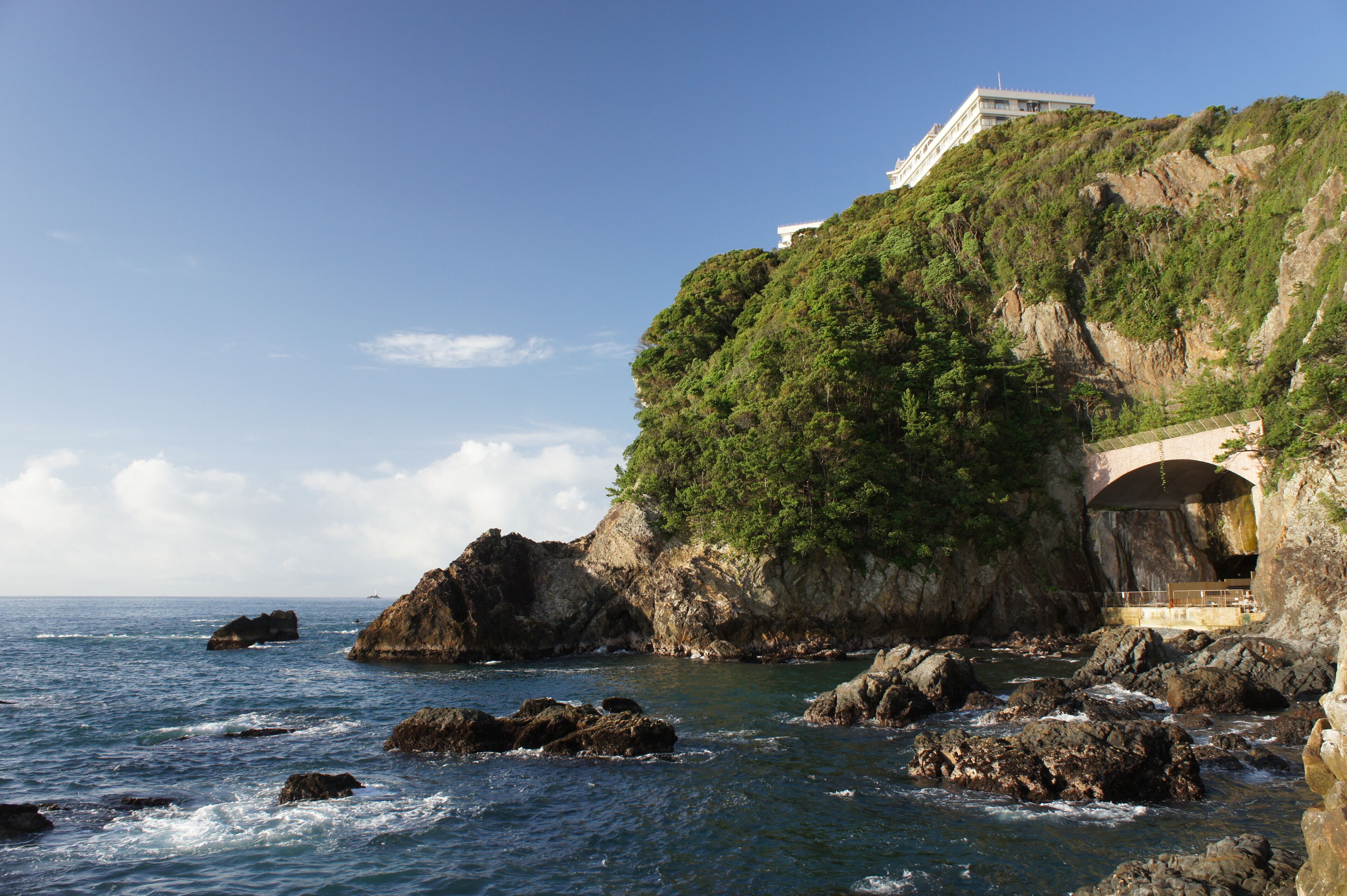 A coastal landscape with rocky outcrops, a bridge, and a building on a cliff.