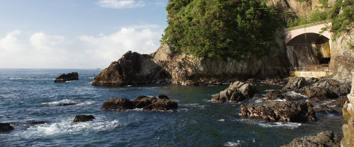 A coastal landscape with rocky outcrops, a bridge, and a building on a cliff.