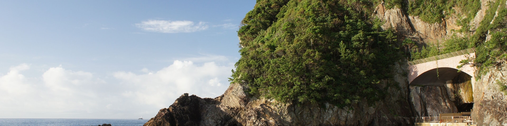A coastal landscape with rocky outcrops, a bridge, and a building on a cliff.
