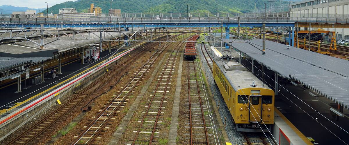 A railway station with multiple tracks and a mountainous backdrop.