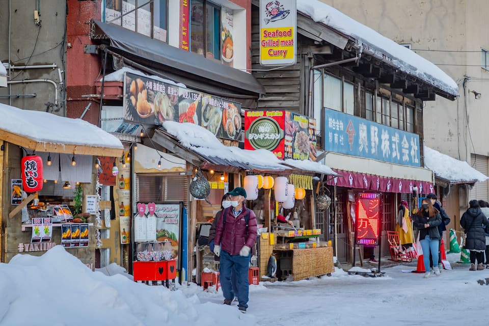 A snowy street with various food stalls and a signboard advertising seafood, grilled meat, and curry.