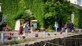 A garden with a green wall, a wooden bench, and people walking.