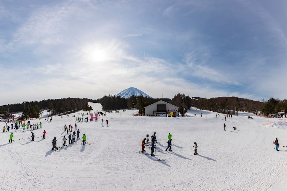 A snowy ski slope with skiers, a mountain in the background, and a building in the middle.