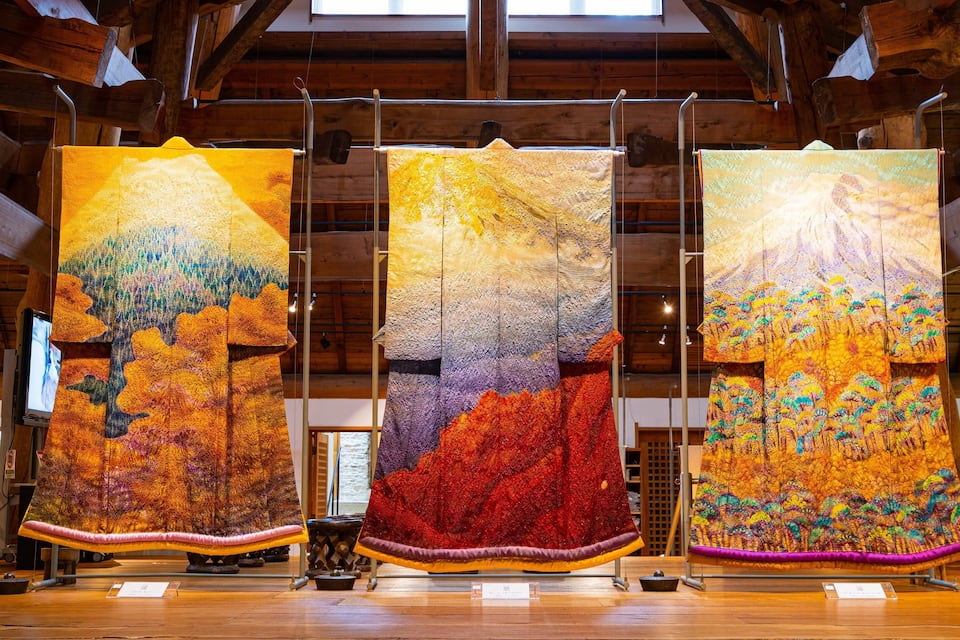 Três grandes tapeçarias penduradas em uma galeria de madeira.