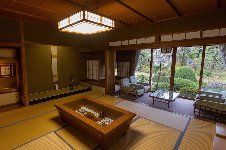 A traditional Japanese room with tatami flooring, a low wooden table, and sliding doors leading to a garden.