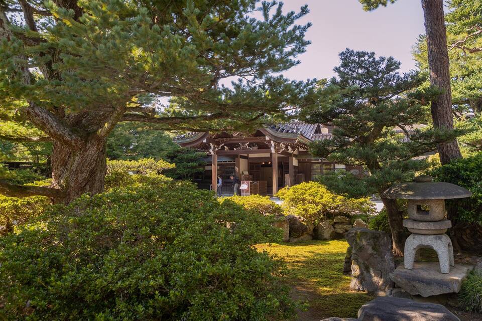 Um edifício japonês tradicional cercado por vegetação exuberante e um candeeiro de pedra.