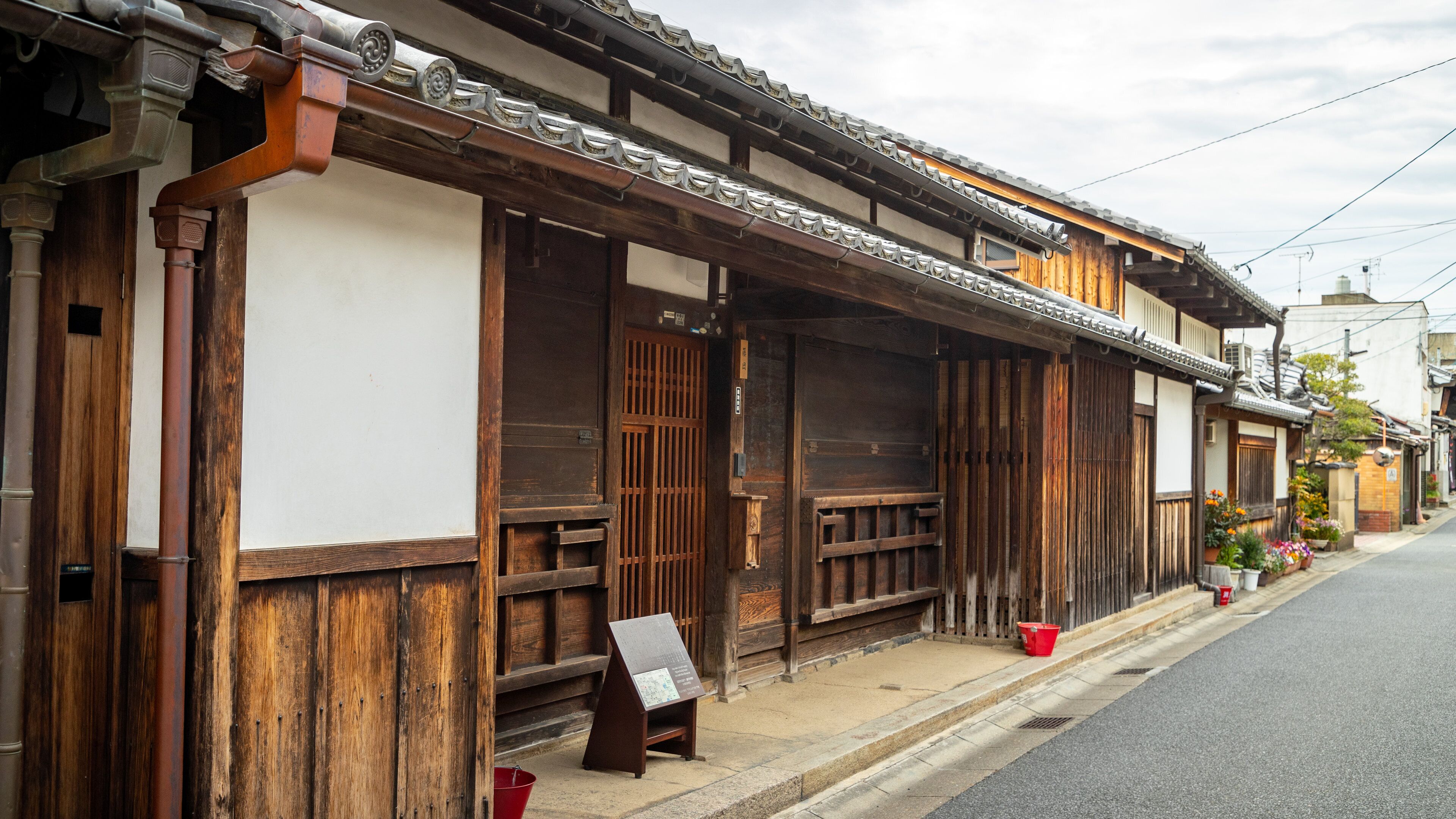 A traditional wooden building with a tiled roof and a signboard on the sidewalk.
