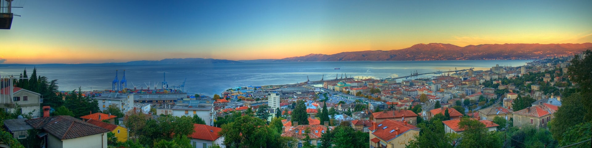 A coastal cityscape with a port, a bridge, and mountains in the background.