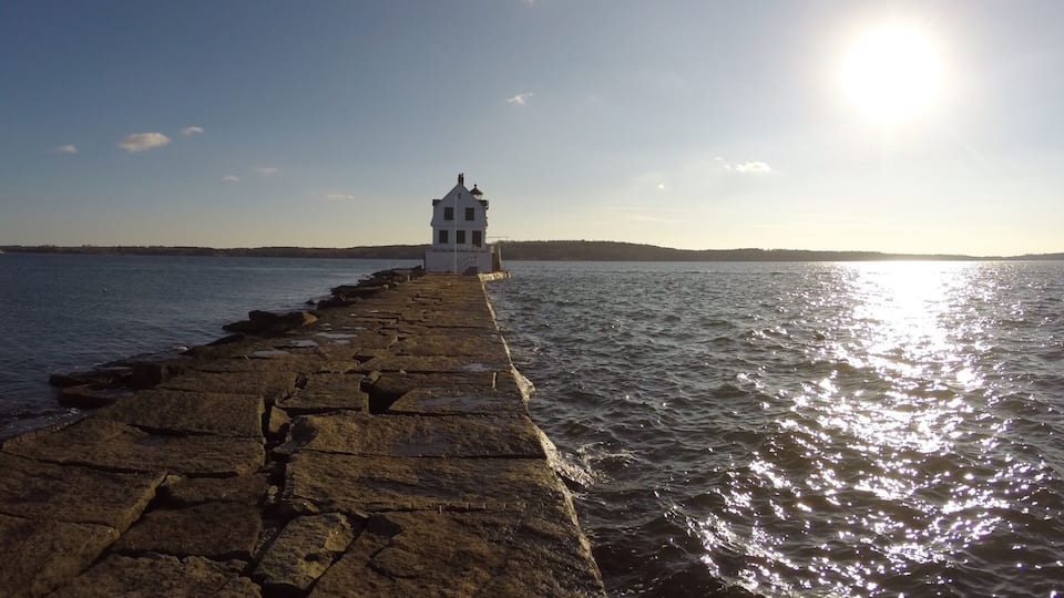 A stone pier leading to a white lighthouse by the sea.