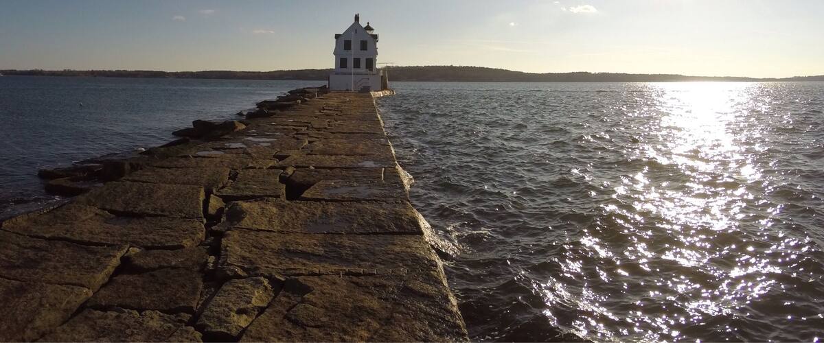 A stone pier leading to a white lighthouse by the sea.