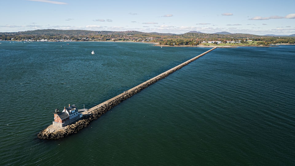 A long pier extending into a calm body of water, surrounded by a hilly landscape with sparse buildings.