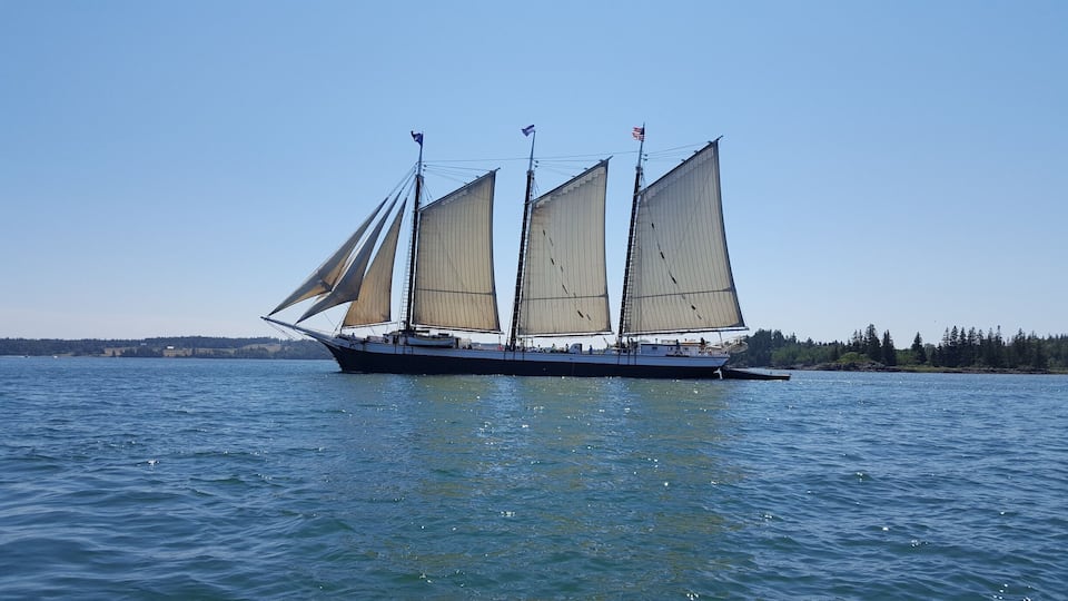 A sailboat with multiple sails on a calm body of water.