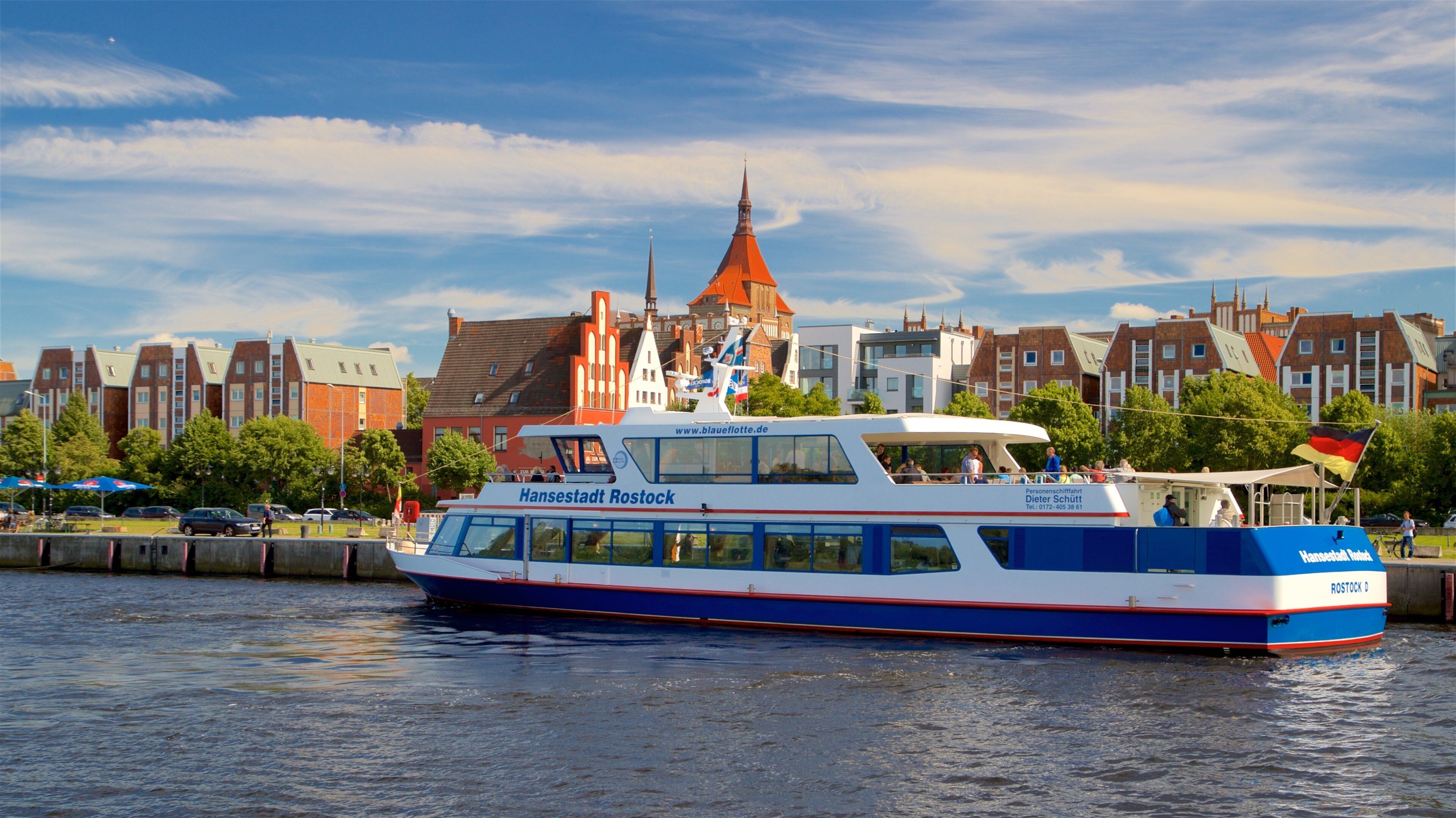 Un barco llamado Hansestadt Rostock en un río, con un paisaje urbano al fondo.