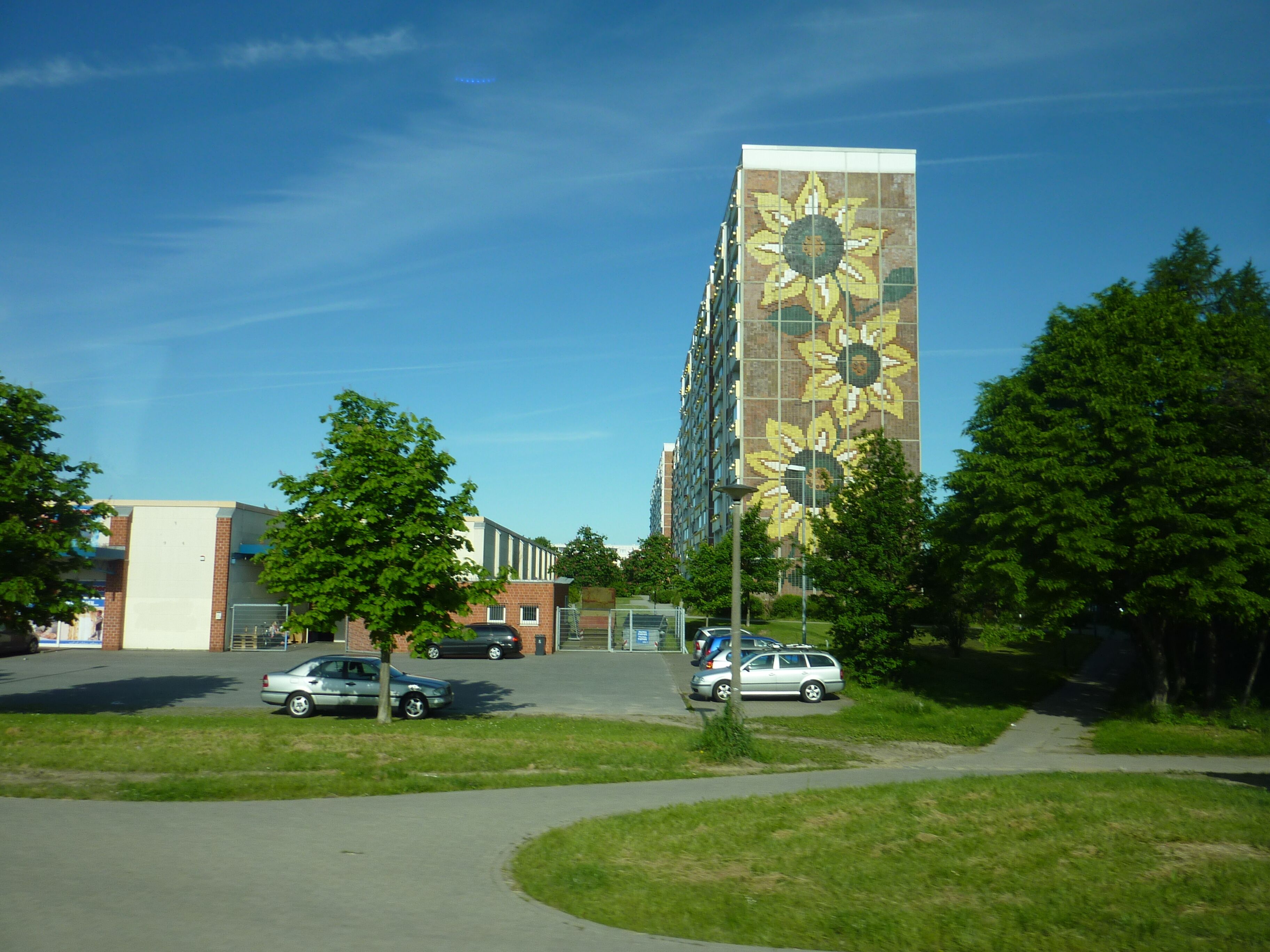 A parking lot with cars, a building with a sunflower mural, and trees.