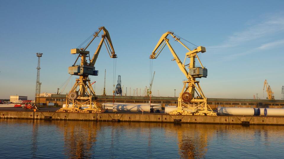 Two large cranes at a port with a calm water body in the foreground.