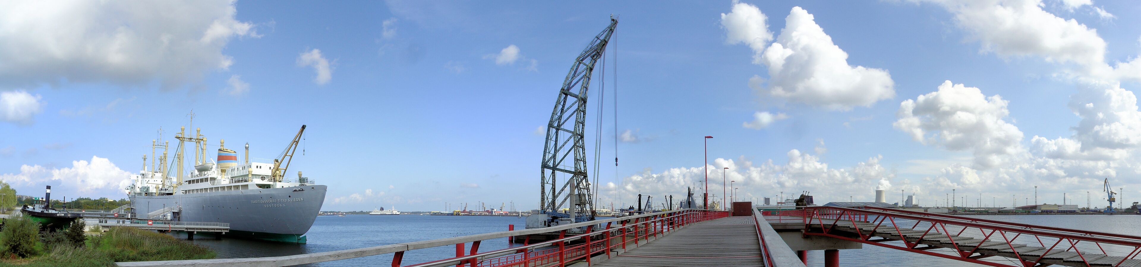 A large ship docked at a port with cranes and a red pier.