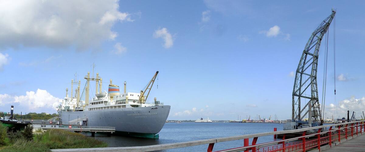 A large ship docked at a port with cranes and a red pier.