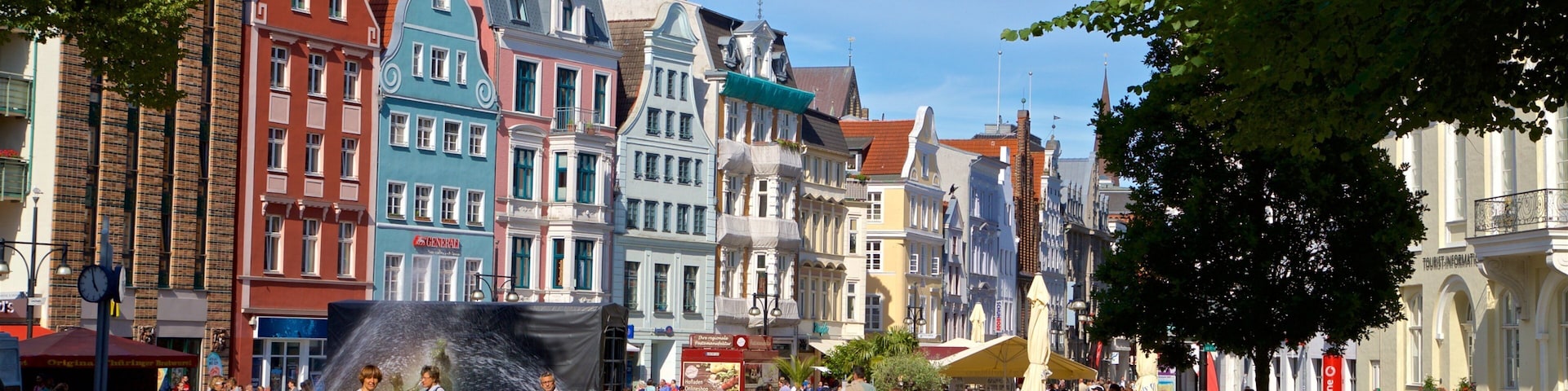 A bustling square with colorful historic buildings, a prominent church spire, and people enjoying the outdoor space.