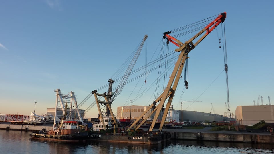 A harbor with multiple cranes and a tugboat named 'ENAK'.