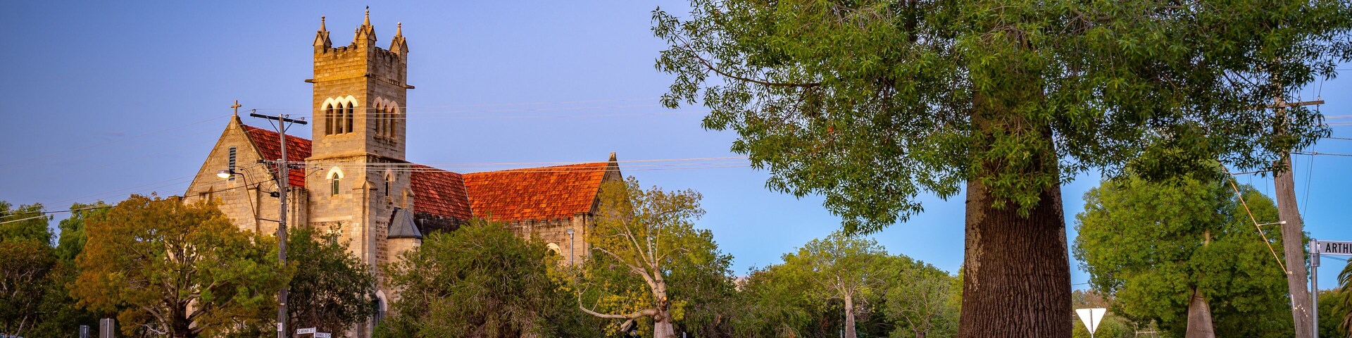 Una iglesia con una torre, rodeada de árboles y un paso de cebra.