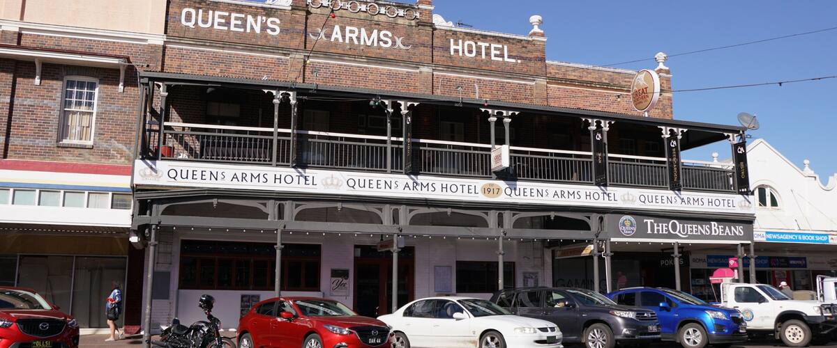 The Queens Arms Hotel with a balcony and parked cars in front.