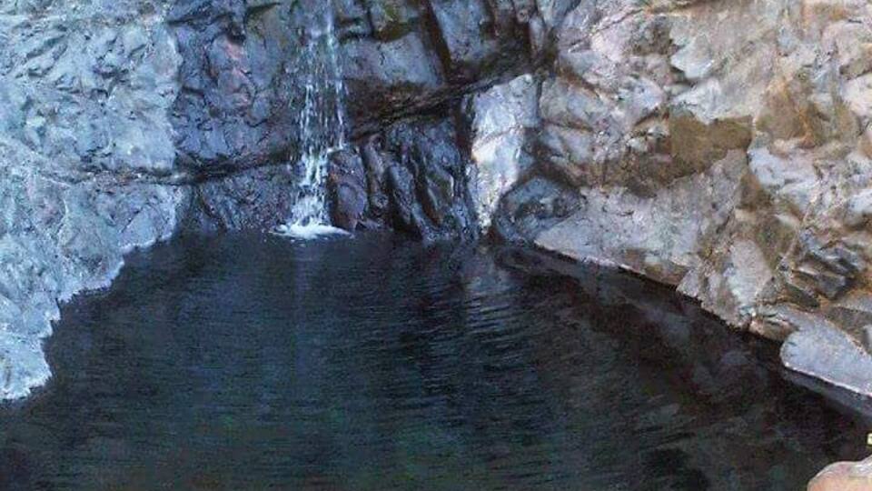 A natural pool with a waterfall, surrounded by rocky terrain.