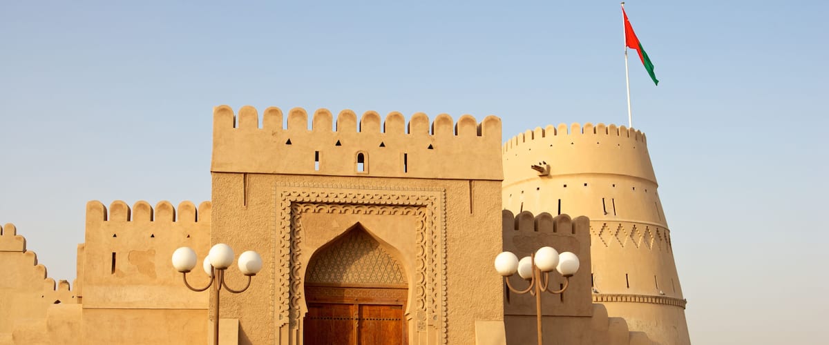 A historic fort with a large wooden door, a flag, and a round tower.