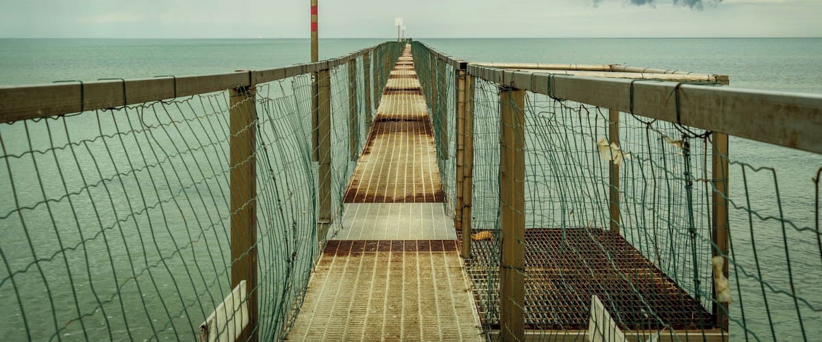 A wooden pier extending into calm waters, surrounded by a wire fence.