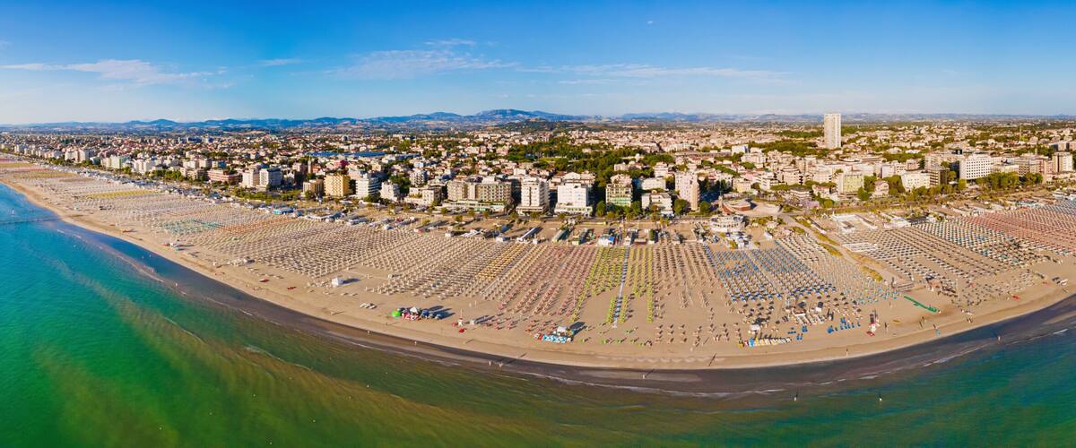 An aerial view of a coastal city with a large beach, dense urban area, and a prominent Ferris wheel.