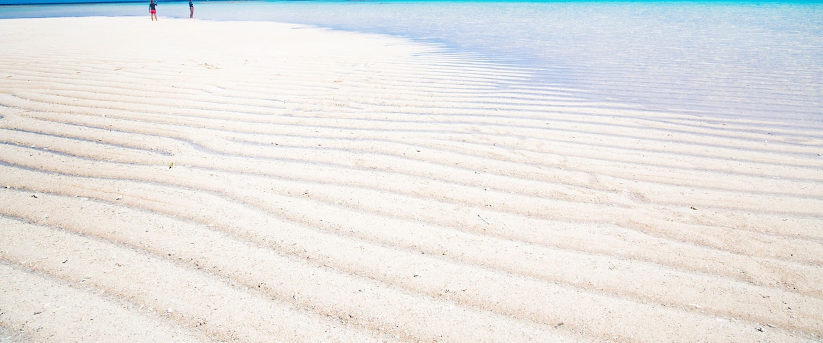A beach with a clear sky and two people walking.