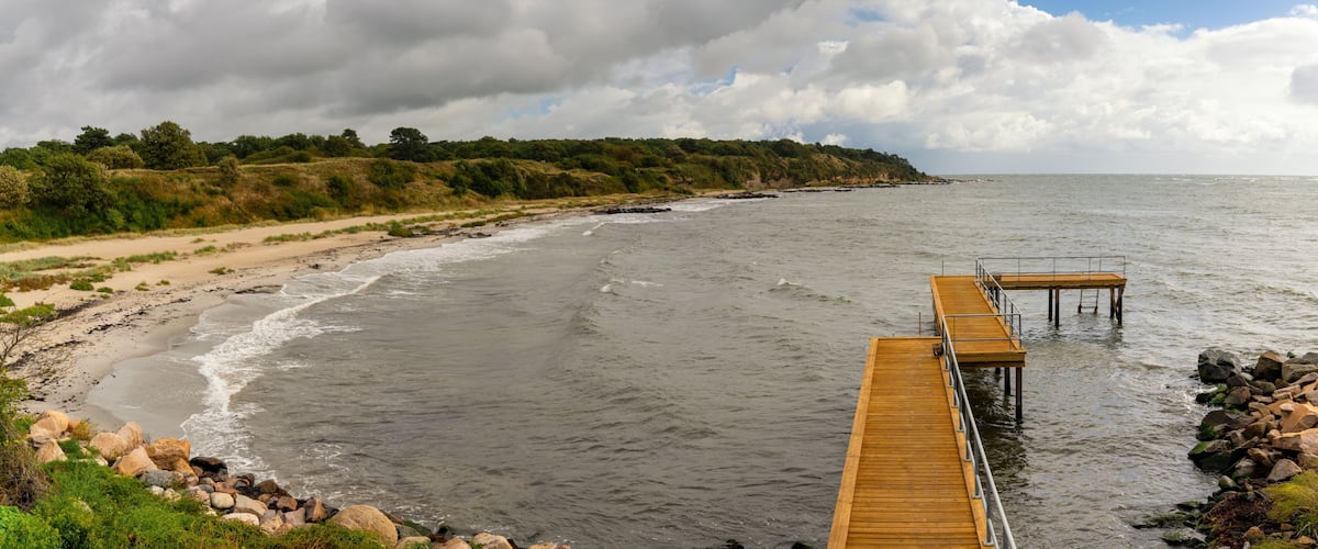 A beach with a wooden pier extending into the water, surrounded by rocky shores and dense greenery.