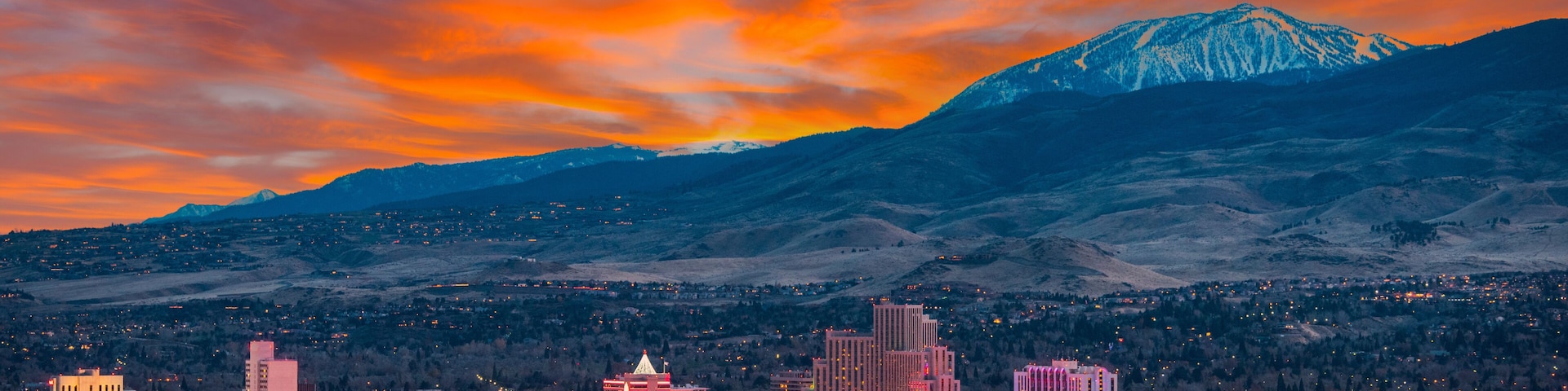 Un paisaje urbano con edificios iluminados y una montaña nevada al fondo.