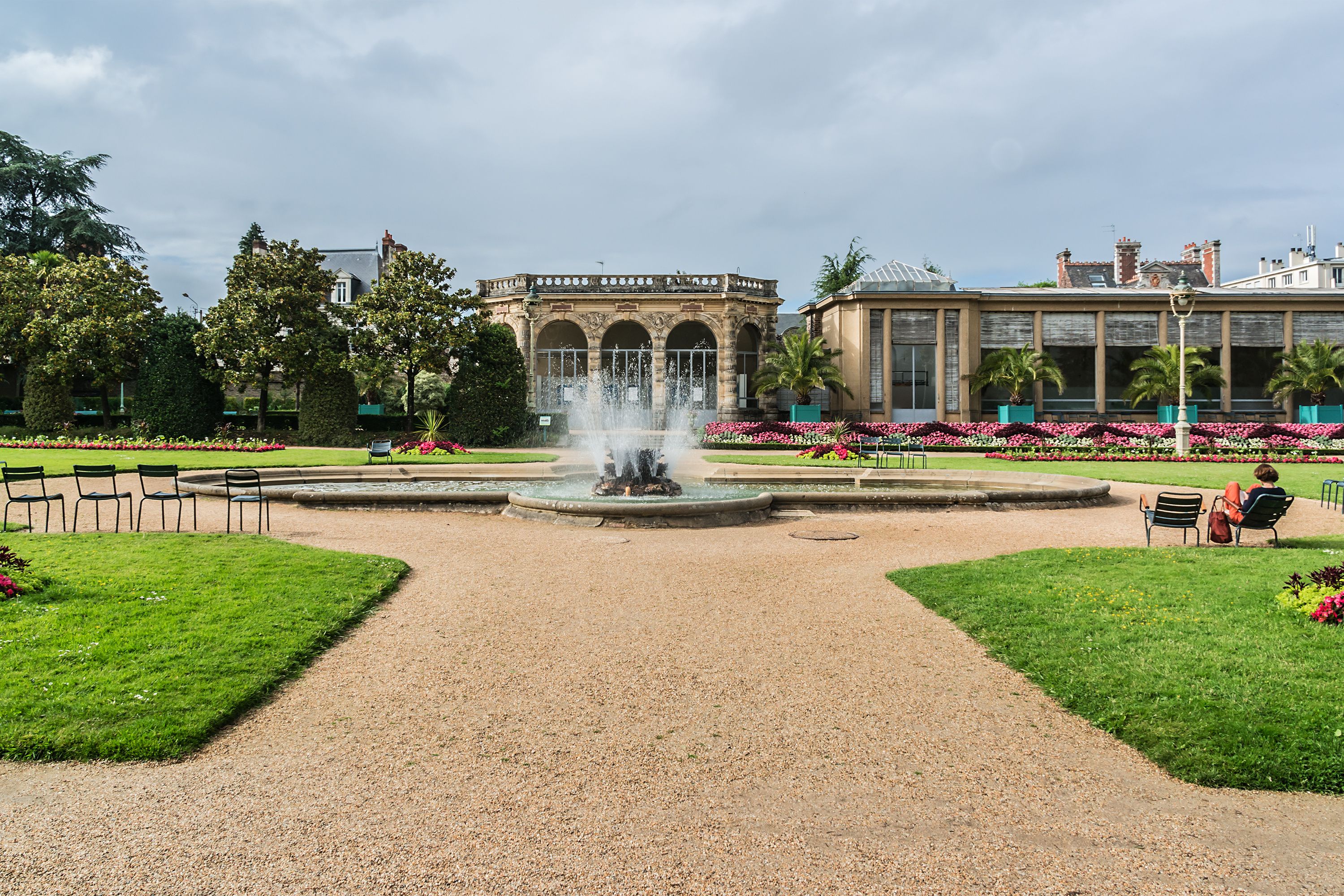 A garden with a fountain, benches, and a building with arched windows.