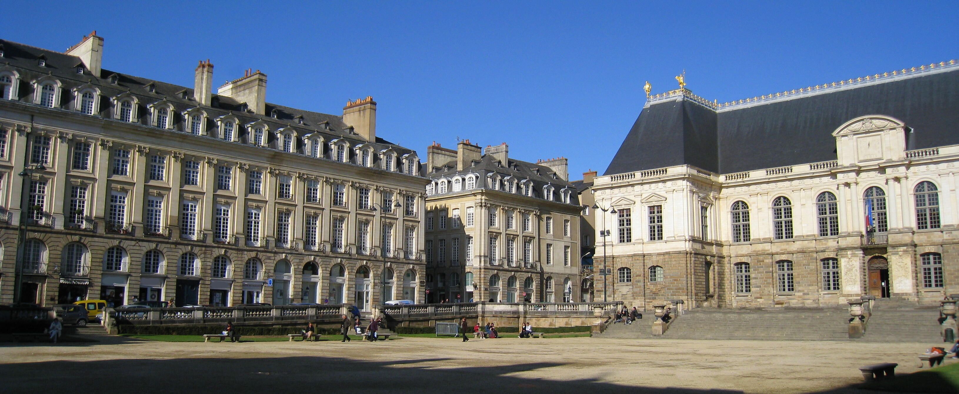 A large historic building with classical architecture, a prominent dome, and a wide open plaza with benches and people.