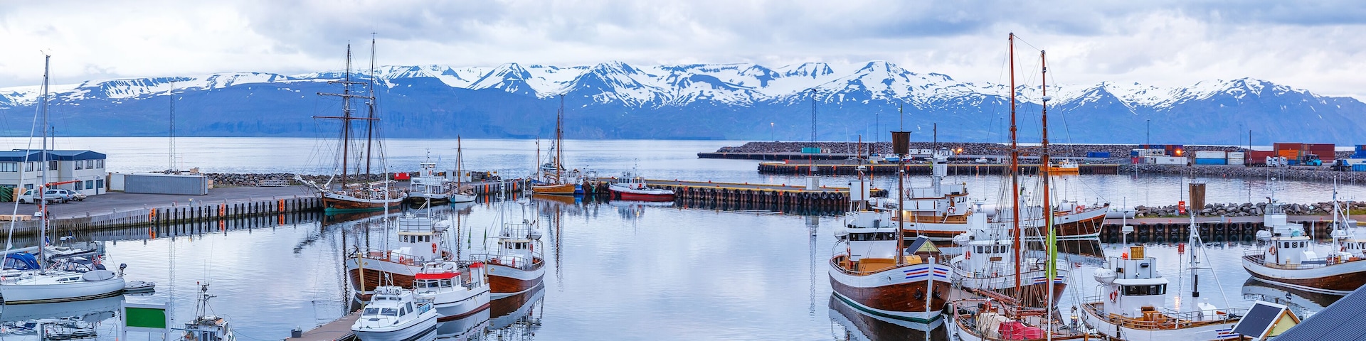 Iceland, Husavic town location. Picturesque panoramic view of northern town Husavik, old harbor with anchored wooden vessels operated for whale watching excursions. Blue hour dusk tranquil scenery.
