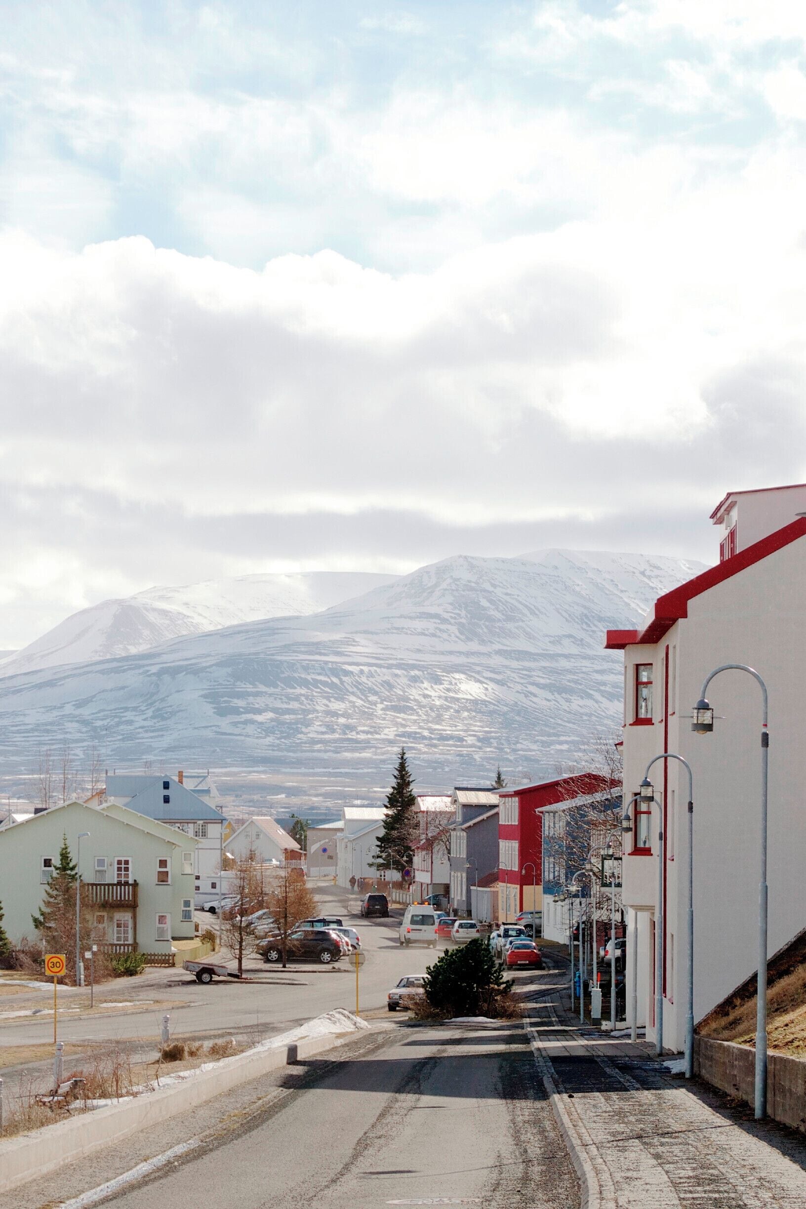 A snow-covered mountain in the background, a street with parked cars, and buildings with red roofs.