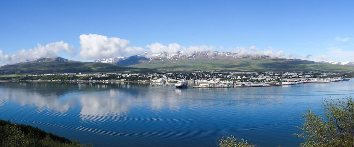 A calm lake with a city and mountains in the background.