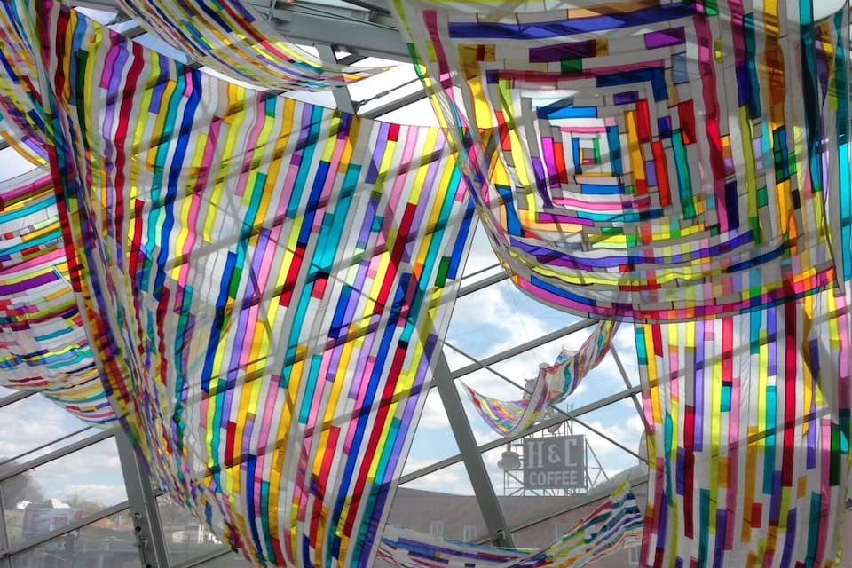 Installazioni di tessuto colorato e a righe all'interno di un edificio con soffitto in vetro.
