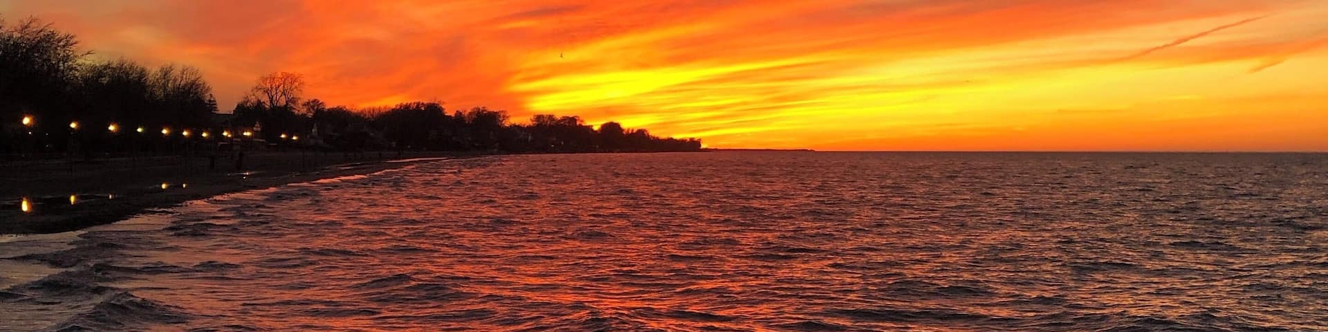 Un atardecer sobre una masa de agua con la silueta de una orilla y farolas.