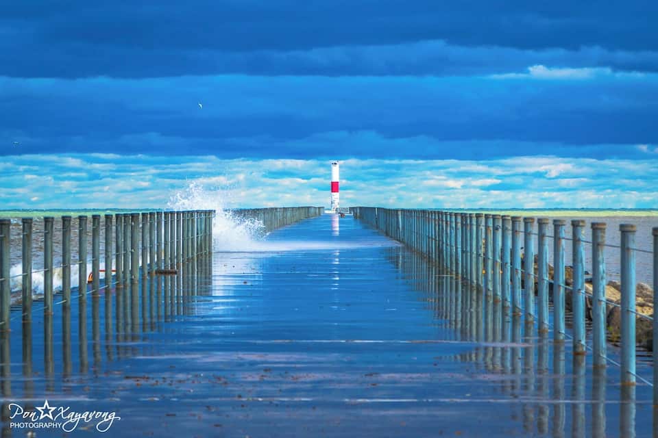 Un muelle de madera se extiende sobre aguas, con un faro rojo y blanco al final.
