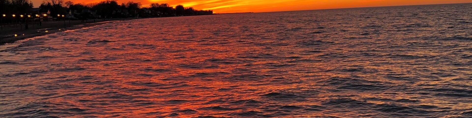 A sunset over a body of water with a silhouette of trees and buildings along the shore.