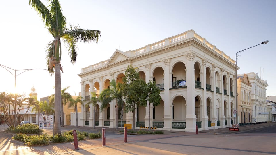 A historic building with arched windows and a balcony, surrounded by palm trees and a street.