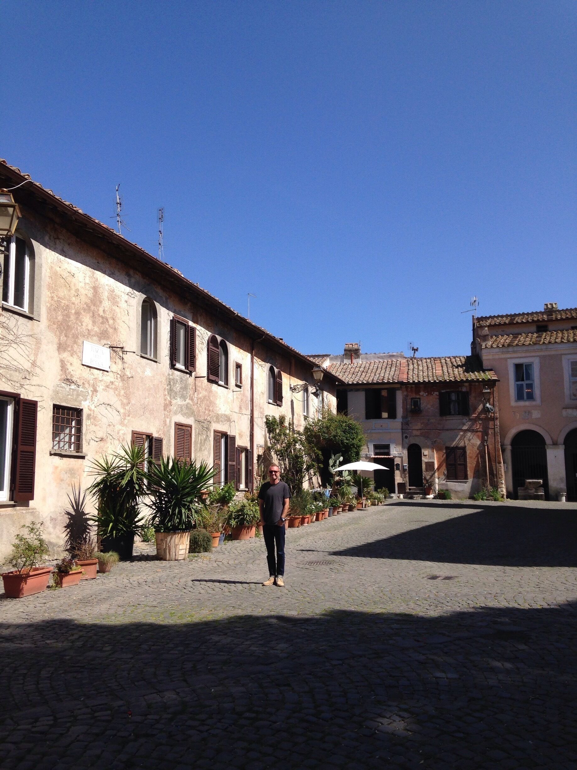 A cobblestone street with historic buildings, potted plants, and a clear blue sky.