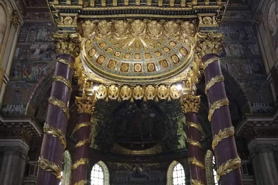 An ornate religious interior with gold and purple columns, a detailed ceiling, and a central altar.