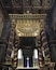 Een versierd religieus interieur met gouden en paarse kolommen, een gedetailleerd plafond en een centraal altaar.