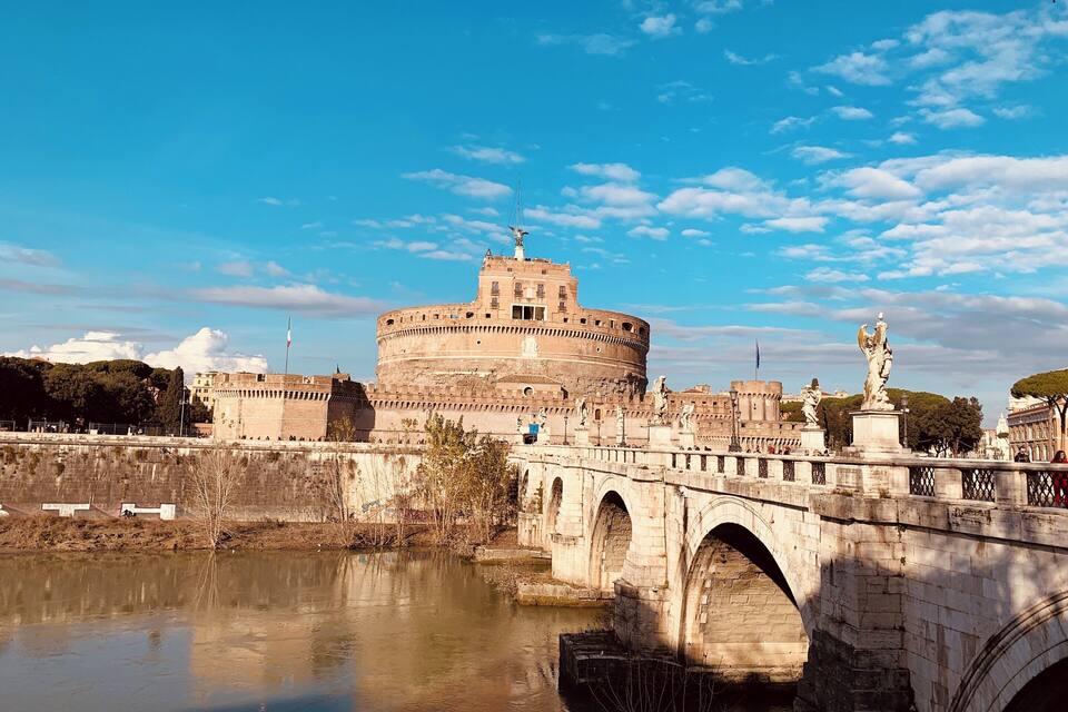 The Colosseum in Rome, Italy, with a bridge in the foreground and a clear blue sky.